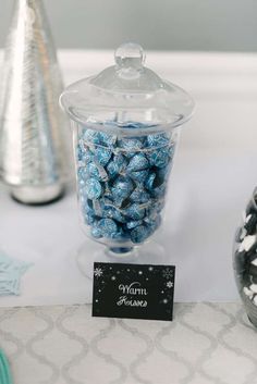 there is a candy jar with blue candies in it and a name tag on the table