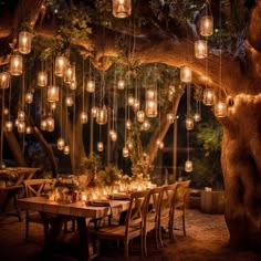 an outdoor dining area with lanterns hanging from the tree and tables set for dinner under them