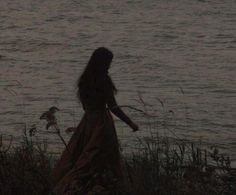 a woman in a long dress is standing by the water at night with her arms outstretched