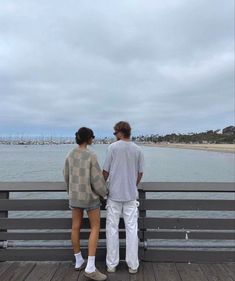 two people standing on a pier looking at the water