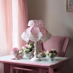 a pink table topped with white vases filled with flowers next to a pink chair