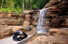 two people ride in an electric vehicle near a waterfall and falls at the same time