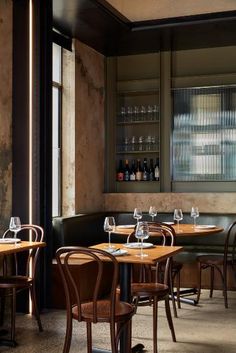 an empty restaurant with wooden tables and chairs in front of a window that has wine glasses on it