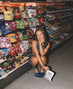 a woman sitting on the ground in front of a store filled with snacks and candy