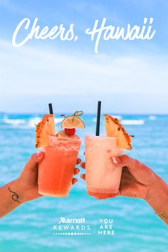 two people holding up drinks in front of the ocean with text that reads cheers, hawaii