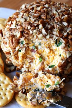 a cheese ball covered in nuts and other toppings with crackers on the side