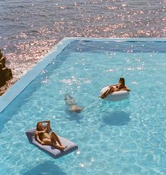 two people floating on inflatable mattresses in a swimming pool next to the ocean