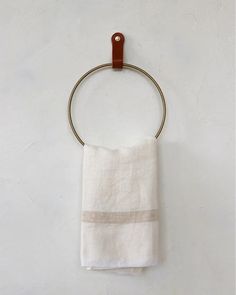 a towel hanging from a metal ring on a white wall with a brown leather handle