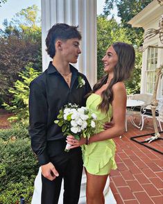 a man and woman standing next to each other on a porch with flowers in their hands