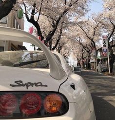 a white car parked on the side of a road with cherry blossom trees in the background