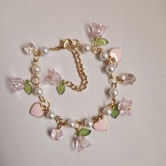 This bracelet is 7.5 inches long with a 2.6-inch extender. It has gold links, pink flower charms with green leaf accents, pink heart charms, and faux pearls. The clasp is a gold lobster clasp. Pink Adjustable Charm Bracelet, Cute Pink Pearl Charm Jewelry, Pink Themed Adjustable Charm Bracelet, Elegant Pink Handmade Charm Bracelet, Whimsical Pink Charm Bracelets, Pink Charm Bracelet, Fairycore Coquette, Pink Charm, Bracelet Inspo