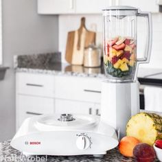 a blender filled with fruit sitting on top of a counter next to a bowl