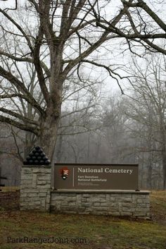 a sign for the national cemetery in front of a tree with no leaves on it