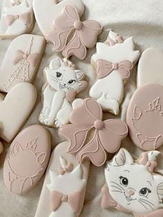 many decorated cookies are laying on a tablecloth with white and pink icing in the shape of cats