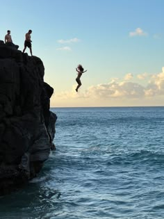 two people jumping off rocks into the ocean from a cliff in the middle of the ocean