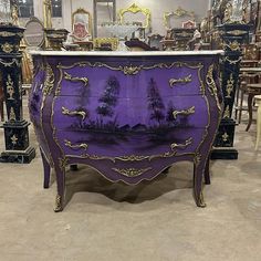 a purple and gold painted dresser with mirrors on the wall behind it in a store