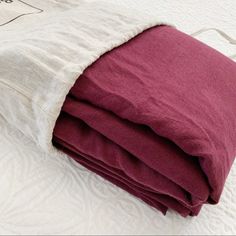 two blankets folded on top of each other in the middle of a bed with white and red sheets