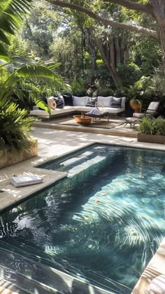 an outdoor swimming pool surrounded by greenery and trees with lounge chairs on the side