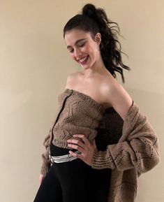 a woman in black pants and a brown sweater posing for the camera with her arms around her waist