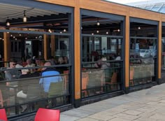 people are sitting at tables in front of the glass doors of a restaurant with red chairs