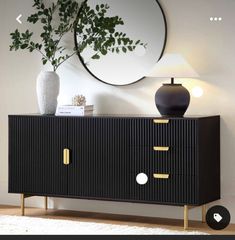 a black and gold sideboard next to a white vase with a plant on it