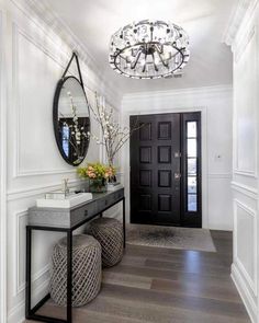 a foyer with a black door and mirror on the wall, two stools under a chandelier