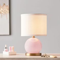 a pink lamp sitting on top of a wooden table next to a white and gold lamp