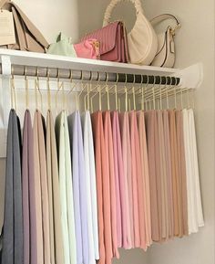 there are many different colored shirts hanging on the clothes rack in this closet, and one is holding a handbag