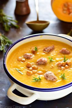 a bowl of soup with meatballs and garnishes on the table next to an orange