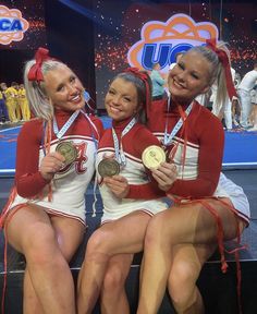 three cheerleaders are sitting on the stage with their medals