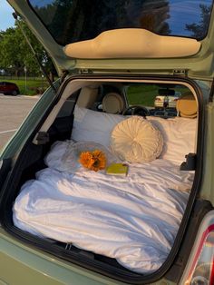 an open hatchback car trunk filled with white sheets and pillows, flowers on the bed