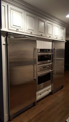 a stainless steel refrigerator and oven in a kitchen with white cabinets on the wall above it