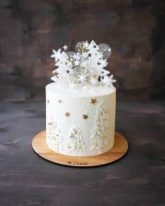 a white frosted cake with gold stars and snowflakes on top, sitting on a wooden platter