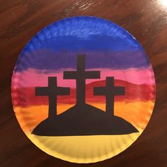 a paper plate painted with three crosses on top of a hill in the middle of sunset