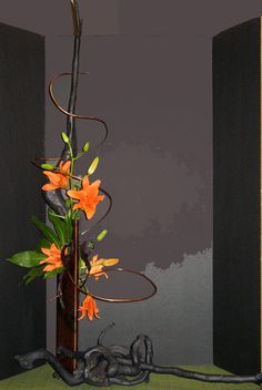 a tall vase with orange flowers in it on a green cloth covered table next to black walls