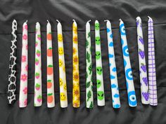 six different colored candles are lined up on a black surface, with faces drawn on them