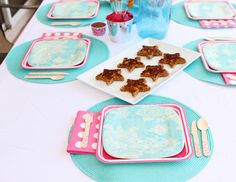 the table is set with blue and pink plates, silverware, and desserts