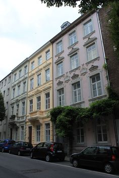 several cars parked on the side of a street in front of tall buildings with ivy covered windows