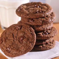 a stack of chocolate cookies sitting on top of a white napkin next to a glass of milk