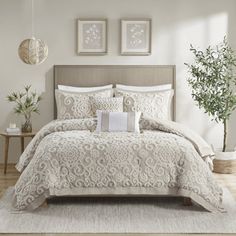 a bed with white comforter and pillows in a room next to a potted plant