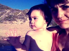 a woman holding a small child in her arms on the beach with mountains in the background