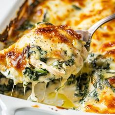 a casserole dish with chicken, spinach and cheese being scooped from it