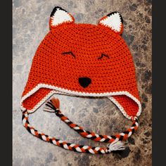 a crocheted red and white hat with an orange fox on it's face