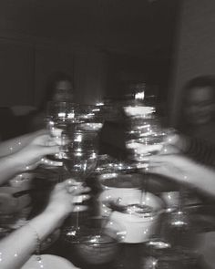 black and white photograph of people holding wine glasses at a dinner table with candles in the middle