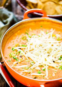 a red pan filled with soup and cheese on top of a wooden table next to chips