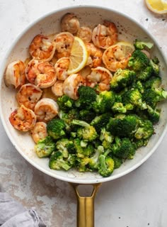 shrimp, broccoli and lemon served in a white bowl with gold serving utensils