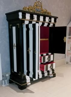 a black, white and red armoire sitting on top of a floor next to a wall