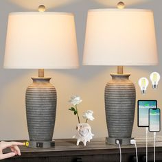 two lamps sitting on top of a wooden table next to a cell phone and flowers