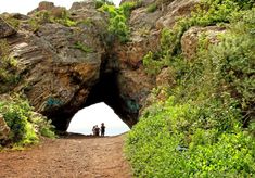 two people are standing in front of an entrance to a cave on the side of a mountain