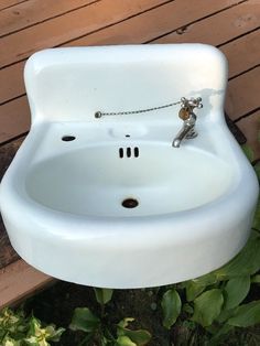 a white porcelain sink sitting on top of a wooden deck next to plants and flowers